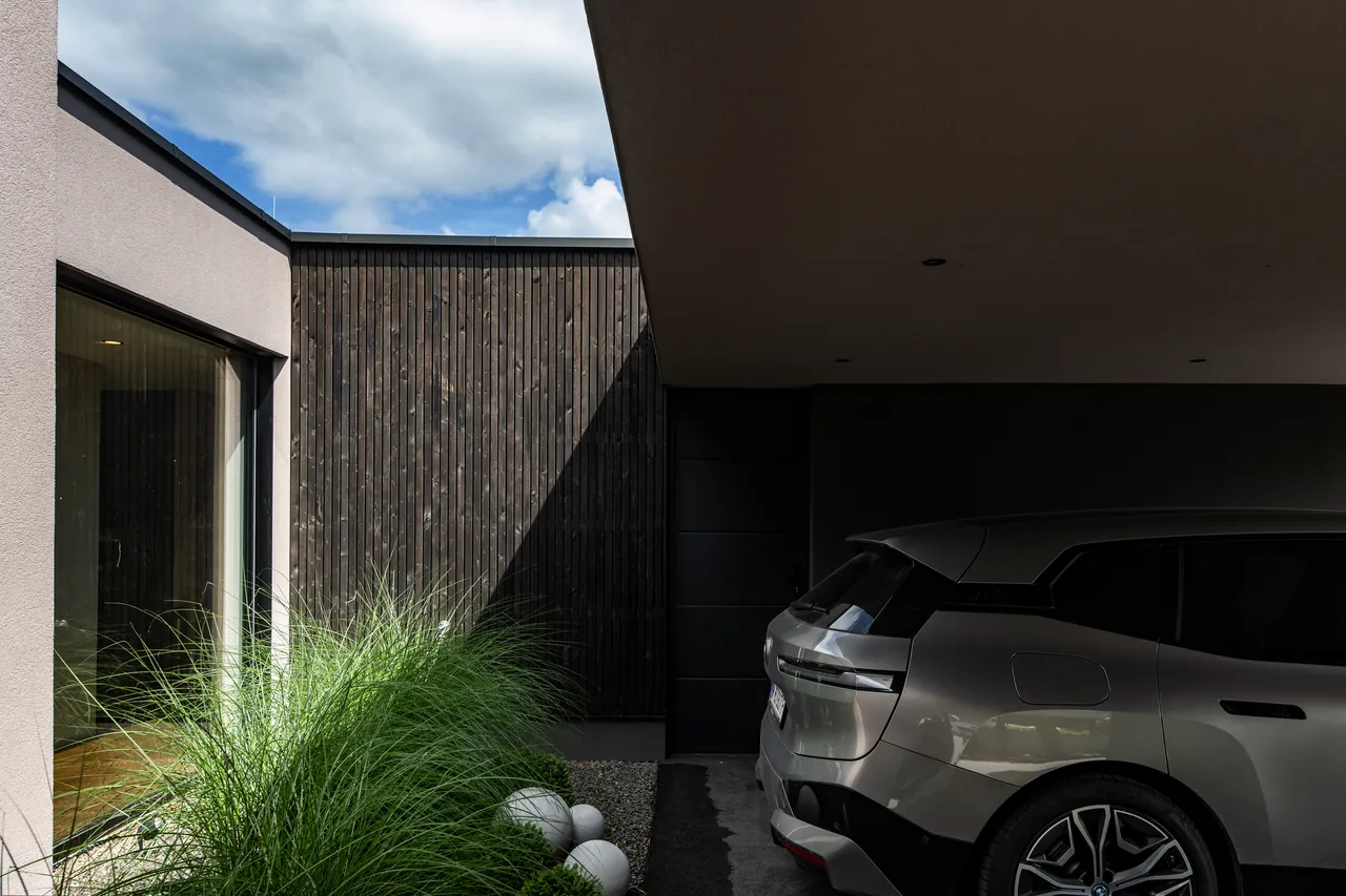 Zufahrt zu Haus L mit Carport und dunkler Holzfassade