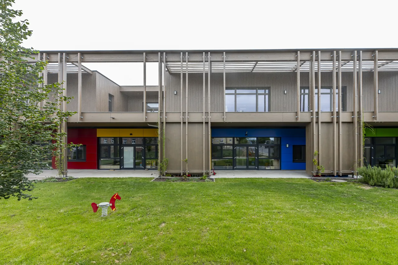 Gartenfassade des Kindergartens mit farbigen Fensterelementen im Erdgeschoss